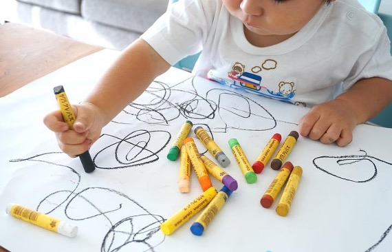 toddler scribbles with crayons at a table