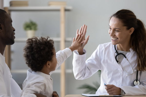 a doctor gives a high-five to a child who is seated in his father's lap