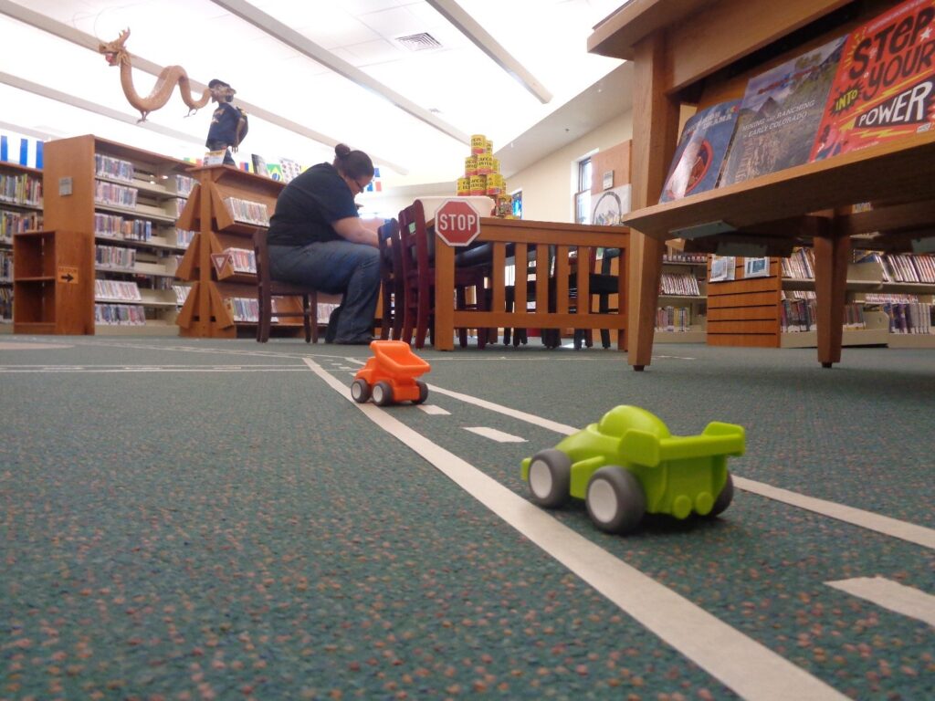 two toy cars on a "road" marked out with masking tape on the carpeted floor of the library