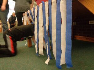 a young child on hands-and-knees crawls through a screen of blue and white strips of crepe paper hanging off the side of a table