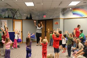 kids standing in a circle around a teacher, all stretching both hands in the air