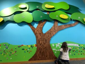 young girl placing magnetic word panels on a wall beneath wooden sculpture of a tree